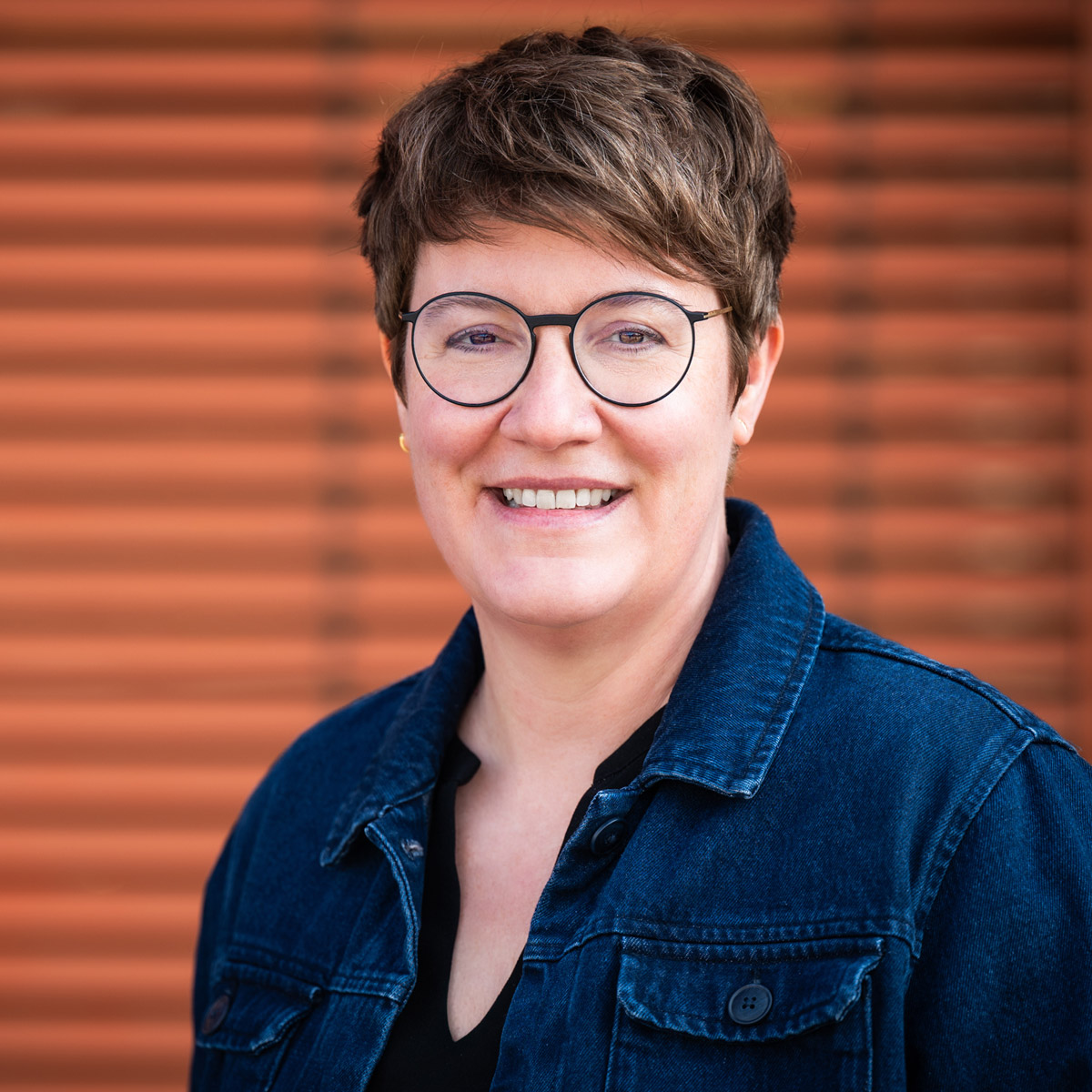 Tina Dingel, Executive Coach und Facilitatorin, lächelt vor einer rostfarbenen Wand im Freien
